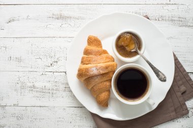 Kruvasan reçel kahve beyaz tahta masada.