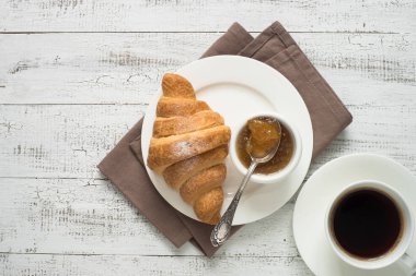 Kruvasan reçel kahve beyaz tahta masada.