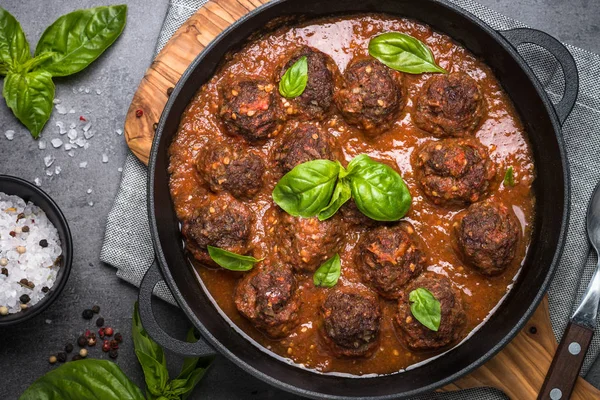 Siyah bir zemin üzerine domates soslu köfte. 