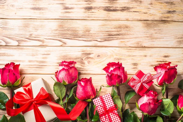 Red rose flower and present box on wooden table.