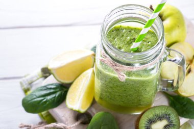 Yeşil smoothie ve malzemelerin üzerine beyaz ahşap masa.