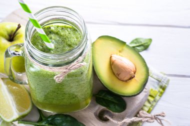 Yeşil smoothie ve malzemelerin üzerine beyaz ahşap masa.