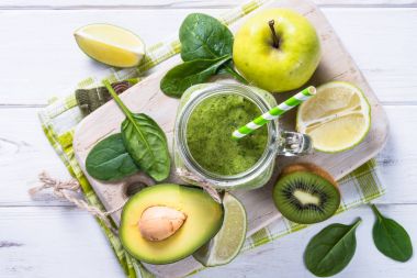 Yeşil smoothie ve malzemelerin üzerine beyaz ahşap masa.