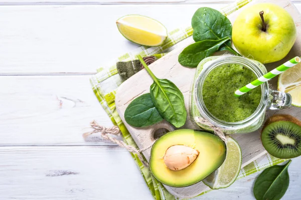 Green smoothie and ingredients on white wooden table. — Stock Photo, Image