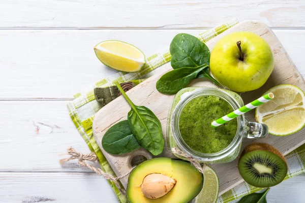 Green smoothie and ingredients on white wooden table. — Stock Photo, Image