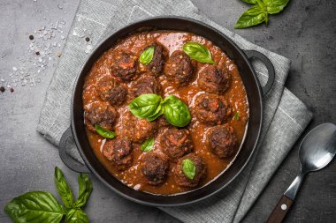 Siyah bir zemin üzerine domates soslu köfte. 