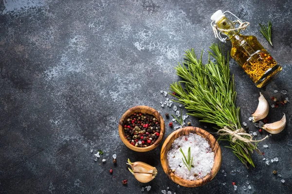 Sprigs of rosemary, pepper and garlic on a dark stone background — Stock Photo, Image