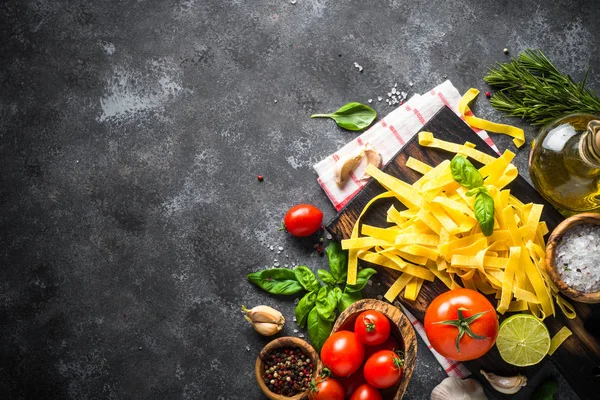 Massas, tomates, queijo, manjericão e azeite sobre a mesa de pedra preta — Fotografia de Stock