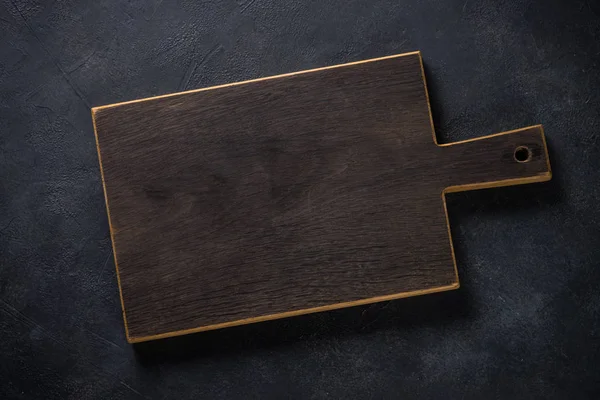 Black wooden cutting board on black table. — Stock Photo, Image