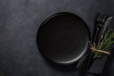 Siyah masa manzaralı beyaz tabak, çatal bıçak ve peçete..