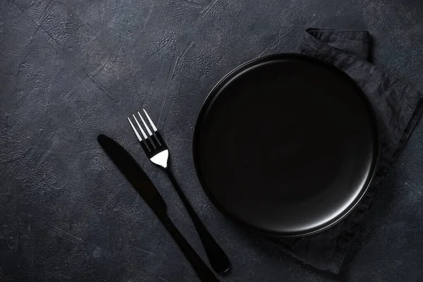 Zwarte plaat, bestek en servet op stenen tafel bovenaanzicht. — Stockfoto