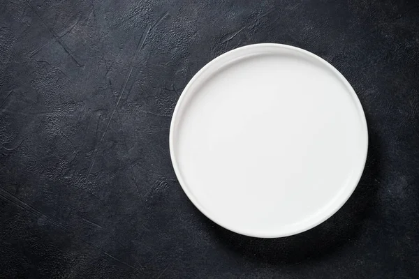 Assiette blanche, couverts et serviette sur table noire vue du dessus. — Photo