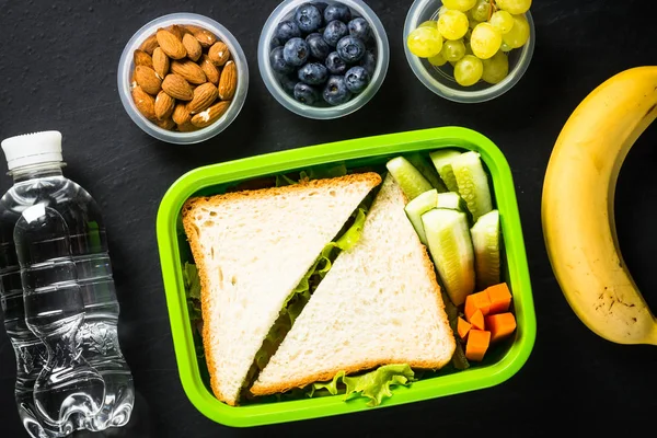 Scatola pranzo con panino e frutta su nero . — Foto Stock