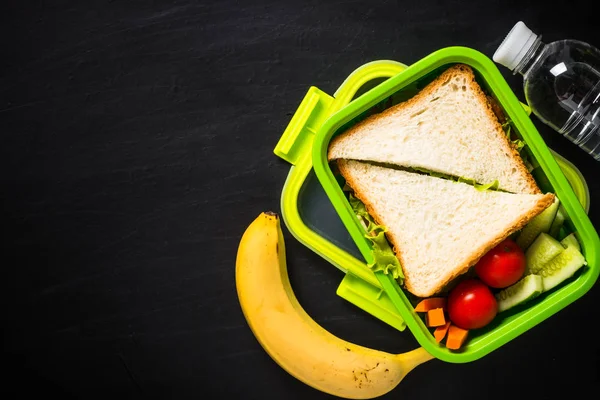 Scatola pranzo con panino e frutta su nero . — Foto Stock