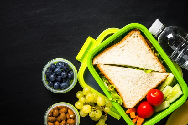 Scatola pranzo con panino e frutta su nero . — Foto Stock