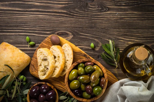 Olives, olive oil and ciabatta on wooden table. — Stock Photo, Image