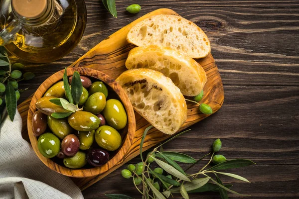 Olives, olive oil and ciabatta on wooden table. — Stock Photo, Image