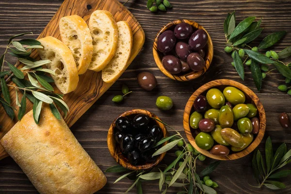 Olivy, olivový olej a ciabatta na dřevěném stole. — Stock fotografie