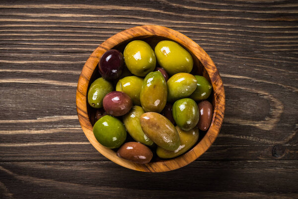 Black and green olives on wooden table.