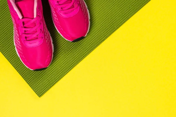 Rosa sneakers och yogamatta på färg bakgrund. — Stockfoto