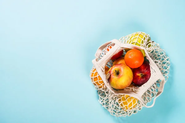 Mesh bag with fruits on color background. — Stock Photo, Image