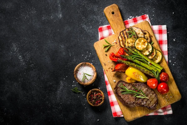 Яловичий стейк на грилі з овочами на чорному кам'яному столі . — стокове фото