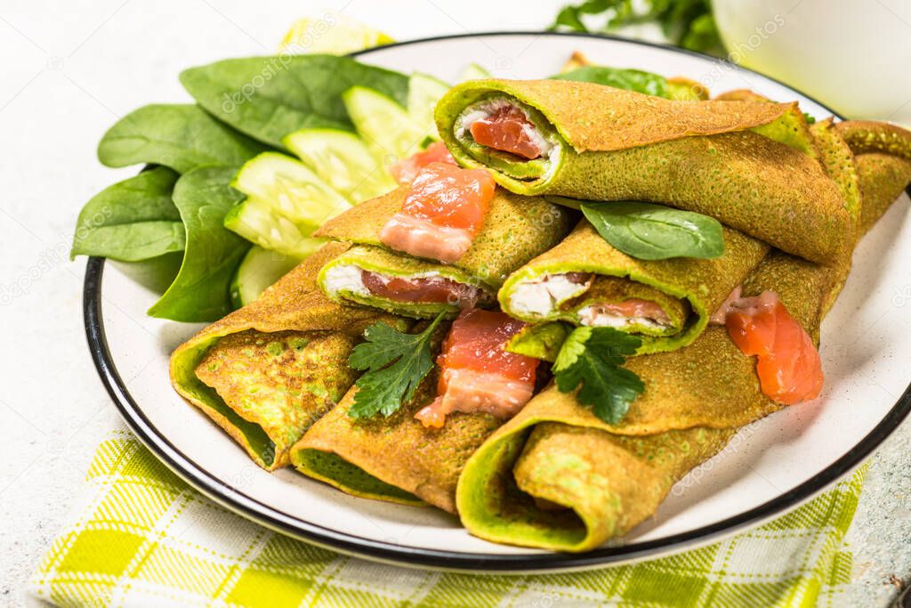 Green pancakes from spinach wrapped with salmon and cream cheese.