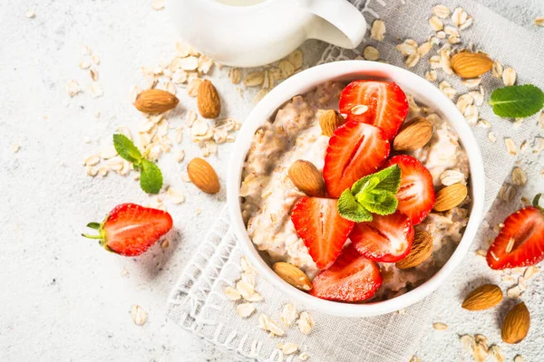 Bubur oatmeal dengan stroberi segar dan kacang pada latar belakang putih. — Stok Foto