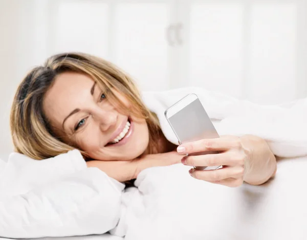 Kadın yatak gülümseyen, yalan bir kısa mesaj okuma — Stok fotoğraf