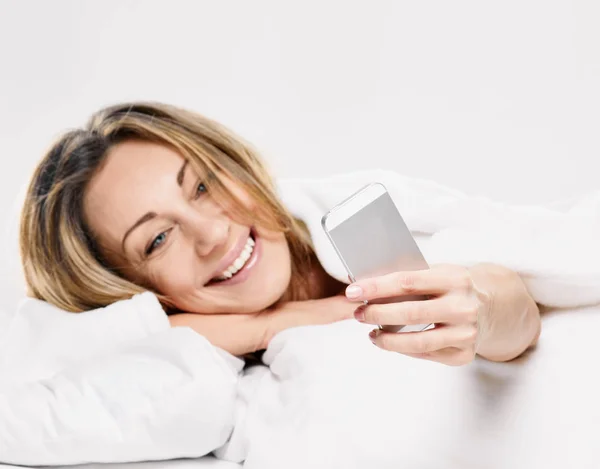 Kobieta, leżąc na łóżku uśmiechnięty, czytanie wiadomości SMS — Zdjęcie stockowe