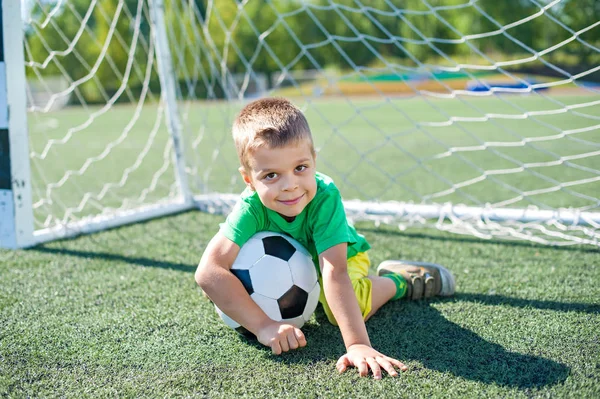 Positiv pojke barn spelar fotboll på fältet. Stockbild