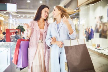 Mutlu bir şekilde sohbet ve holding kağıt gülümseyen alışveriş merkezinde alışveriş iki güzel kadın portresi ile alışveriş torbaları
