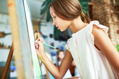 Yetenekli güzel kız Boyama resim arka planda diğer çocuklarla resim dersinde şövale üzerinde yan görünümü portresi