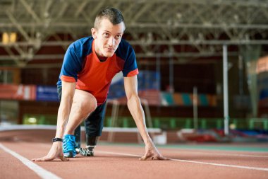 Motivasyon genç amputee atlet modern kapalı stadyum içinde koşu parkuru üzerinde başlangıç konumda portresi