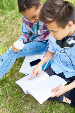 İki öğrenci, erkek ve kız, yeşil çim kitap ve kahve fincanı ile birlikte oturan eğitim yüksek açı portresi