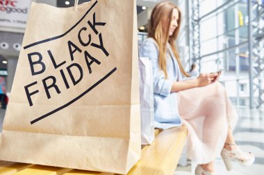 Alışveriş Merkezi tezgah, odakta geri Black Friday kağıt üzerinde otururken smartphone kullanarak moda genç kadın portresi