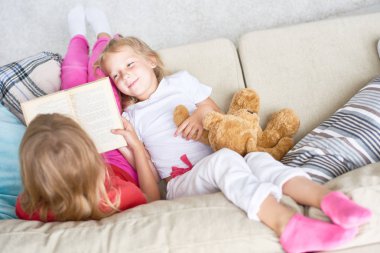 Evde eğlenmek: rahat koltukta yalan ve o yüksek sesle, masal okuma sırasında ilgi ile onun en iyi arkadaşı yüksek açılı görünüş dinlerken sevimli küçük kız