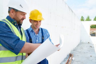Neşeli grup son derece profesyonel inşaat işçileri Koruyucu baretler verimli tartışma planı, bitmemiş arka plan üzerinde binanın iç giyim