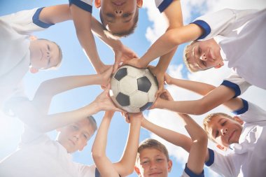 Daire holding topu birlikte ayakta ve kamera karşısına mavi gökyüzü bakarak genç futbol takımı çocuklardan düşük açılı görünüş