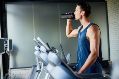 Kendini spor salonunda, profil görünümü koşu bandı üzerinde çalıştırırken su ile yenileme kulaklık konsantre sporcu