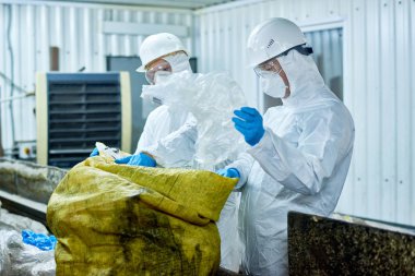 Portre biohazard giyen iki işçilerin çalışma sıralama Konveyör bant üzerinde geri dönüşümlü plastik atık işleme tesisinde uygun