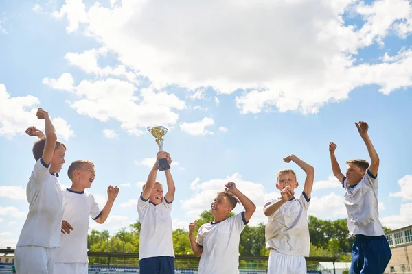 Portrait of boys in junior football team cheering happily and jumping holding trophy cup after winning match