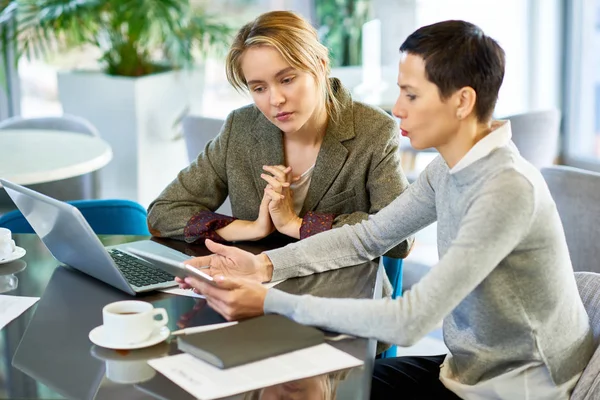 Portrait of two businesswomen discussing work and using laptop during business meeting in modern office