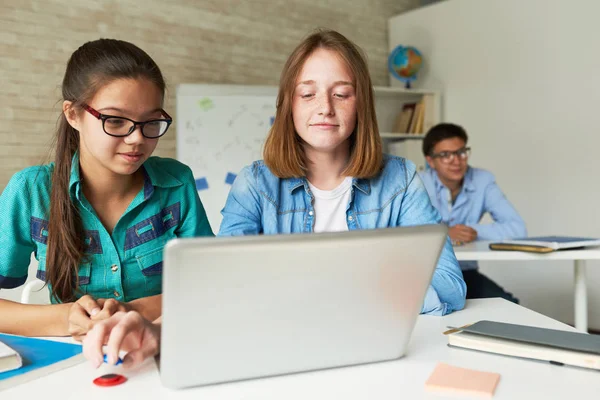 聪明的十几岁的学生穿着休闲服使用笔记本电脑 Ict 他们的男同学在眼镜坐在他们身后 看着相机 — 图库照片