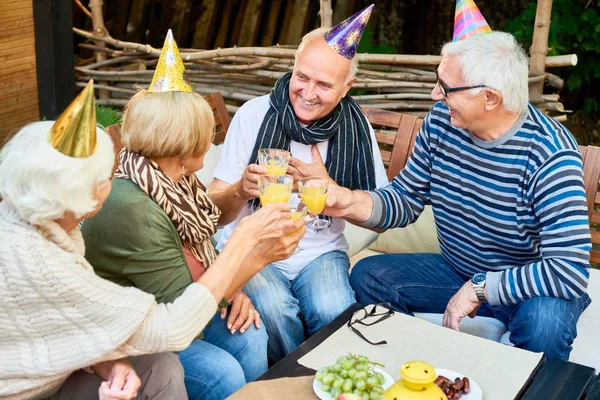在户外咖啡馆庆祝生日的时候 戴着派对帽的微笑老人的画像和一群朋友一起举杯祝酒 — 图库照片