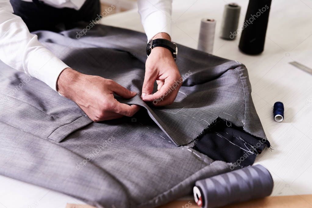 Production process of custom-made male jacket: unrecognizable tailor concentrated on sewing with needle and thread, close-up shot