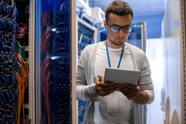 Süper mavi ışık ile çalışırken sunucu kabine tarafından dijital tablet ayakta kullanan modern genç adam portresi