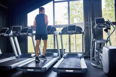 Treadmill egzersiz yaparak ve modern bir spor salonu panoramik pencerelerden güzel manzarayı kaslı sporcu arkadan görünüm