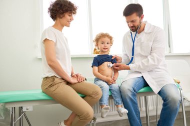 Portre sevimli küçük çocuk ziyaret Doktor, cesur arıyorsunuz ve gülümseyen, çocuk doktoru kalp atışına stetoskop ile dinleme süre