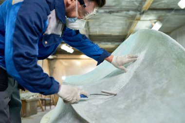 Unrecognizable mature man wearing protective mask repairing boat while working in yacht workshop, covering boat with pre-paint base coating,  copy space clipart